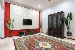 Un soggiorno con televisione a schermo piatto, mobiletto in legno scuro e tappeto decorato.