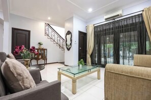 A living room with a sofa, a glass coffee table, a staircase, and a view through a window with curtains. - Kota Damansara ICozy Cove Homestay 10 Pax (Petaling Jaya)