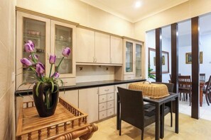 A modern kitchen with wooden cabinets, a dining area with a table and chairs, and a vase with purple flowers on a wooden tray. - Kota Damansara ICozy Cove Homestay 10 Pax (Petaling Jaya)