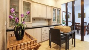 A modern kitchen with light-colored cabinets, a wooden dining table with a woven centerpiece, and purple flowers in a vase.