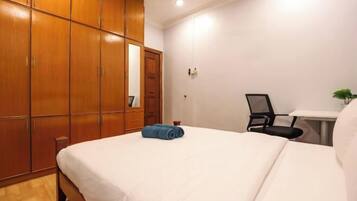 A bedroom with a bed, a wooden wardrobe, a desk with a chair, and a small potted plant.