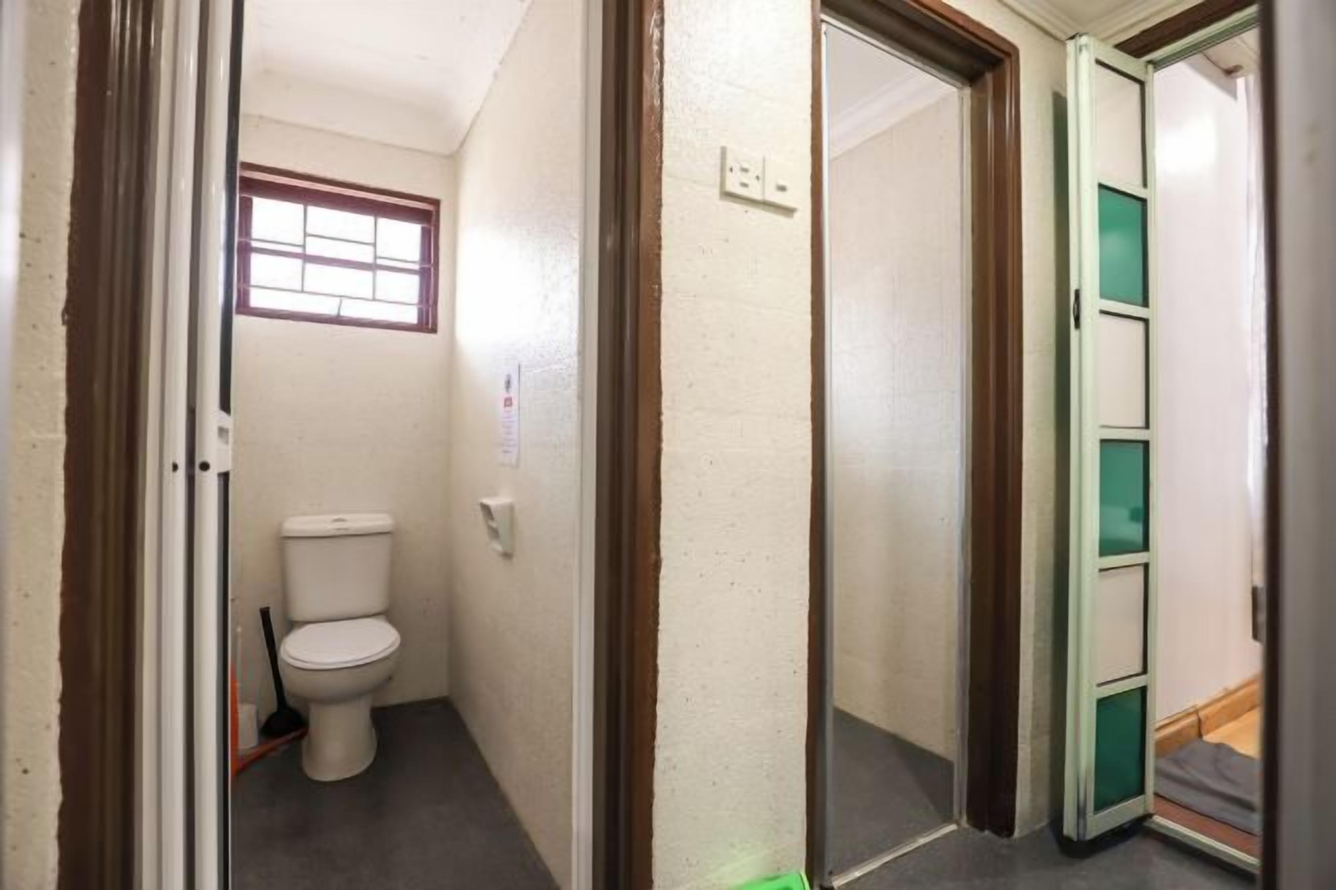 A narrow hallway with a toilet on the left, a door with a green panel on the right, and a window above the toilet.