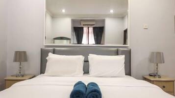 Une chambre d’hôtel avec un grand lit, deux oreillers blancs, une tête de lit, une table de chevet avec une lampe, un miroir au-dessus du lit et une fenêtre avec des rideaux.
