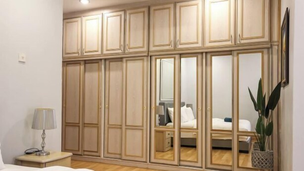 A bedroom with a large wardrobe, a bedside table with a lamp, and a potted plant.