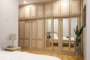 A bedroom with a large wardrobe, a bedside table with a lamp, and a potted plant. - Kota Damansara ICozy Cove Homestay 10 Pax (Petaling Jaya)