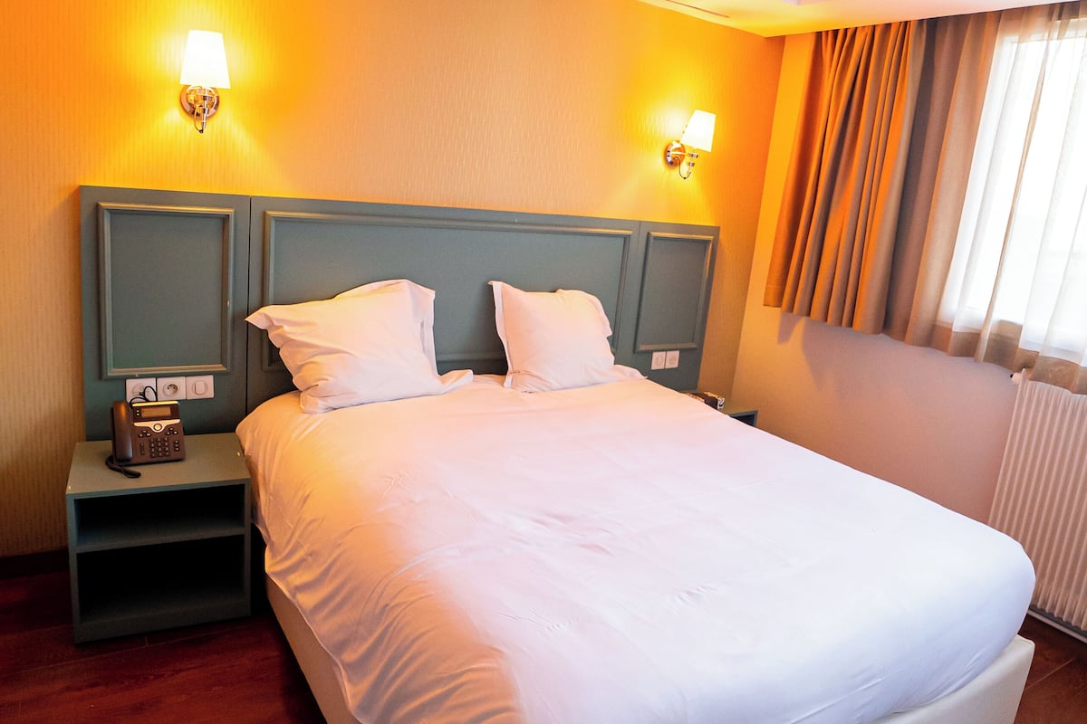 A hotel room with a large bed, two bedside lamps, a nightstand, and a wooden floor.
