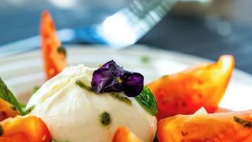 A plate with a scoop of white food, possibly ice cream, garnished with a purple flower and surrounded by sliced tomatoes and greens.