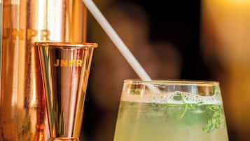 Ein Cocktail mit Strohhalm, ein Messing-Cocktailshaker und ein Glas auf einer spiegelnden Oberfläche.