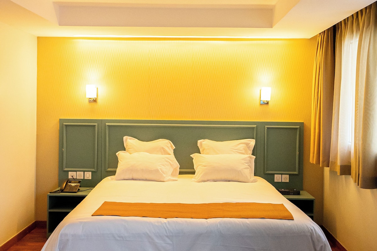 A hotel room with a large bed, two bedside tables, a nightstand, and a wall-mounted light fixture.