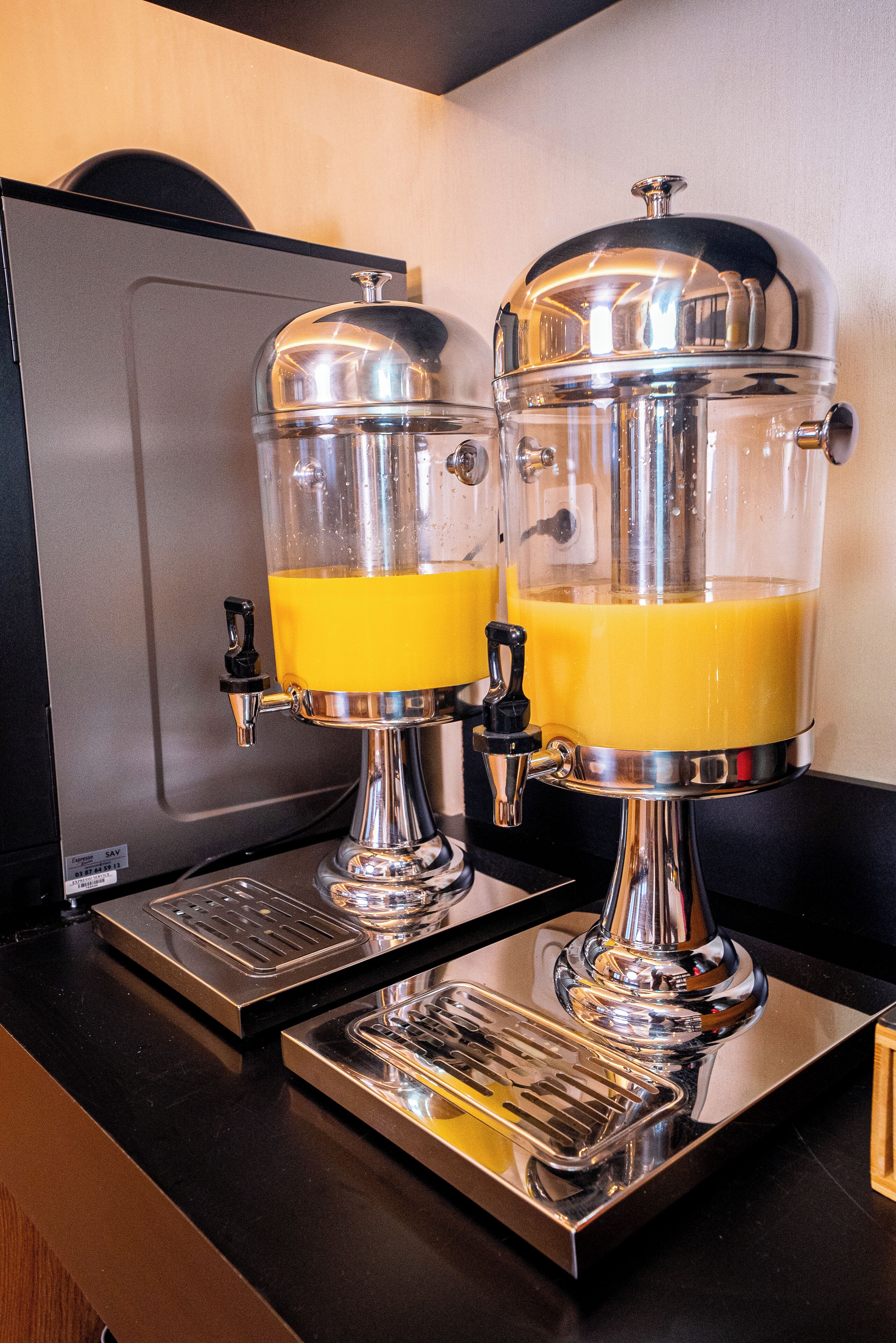 Two juice dispensers with transparent containers and metallic tops, placed on a black countertop.