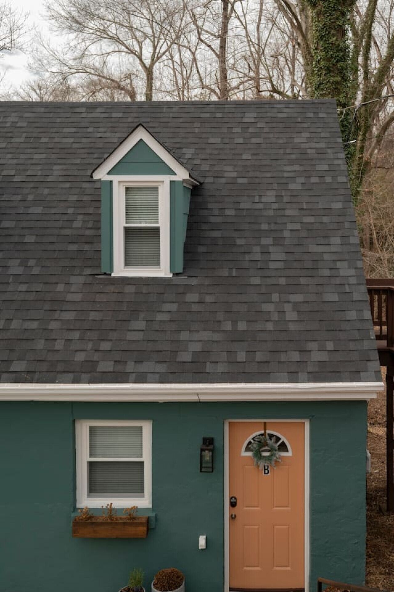 Une maison à deux étages, avec une façade vert foncé, une porte marron et une petite fenêtre de toit agrémentée de volets.