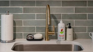 A kitchen with a stainless steel sink, a gold faucet, a soap dispenser, and a paper towel holder. - *Whole House* | 4-BR Home | 2 Kitchens + Free WiFi (Lynchburg)