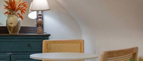 A small, cozy room with a round table and two chairs, a teal cabinet, and a lamp.