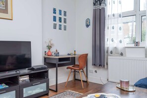 A living room with a TV, a desk, a chair, and a window with curtains.