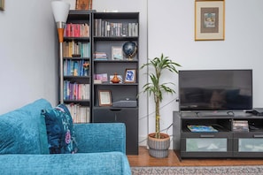 En stue med en sofa, en bogreol, et fjernsyn og en potteplante.