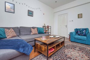 Un salon avec un canapé gris, un fauteuil bleu, une table basse en bois et un tapis à motifs.