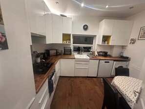Una cocina compacta con alacenas blancas, estufa, fregadero y lavavajillas.