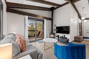 A modern living room with a sofa, a television, a fireplace, and a sliding glass door leading to an outdoor area.
