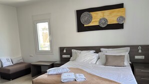 Ein ordentlich eingerichtetes Hotelzimmer mit einem großen Bett, einem Nachttisch, einem kleinen Schreibtisch, einer Bank und einem Fenster.