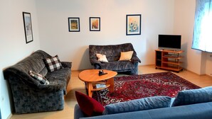 A living room with two sofas, a coffee table, a TV on a wooden stand, and a patterned rug. - For companies only! Comfortable apartment for fitters near Gießen with own entrance. (Reiskirchen)
