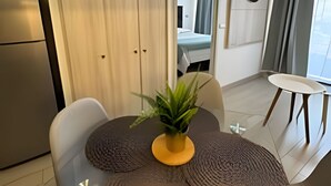 A modern living room with a round table, a sofa, and a potted plant. There is a sliding door leading to a bedroom with a bed and an air conditioning unit on the wall. - NR APART TOCORNAL (Santiago)