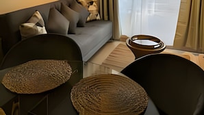 A modern living room with a grey sofa, a black chair, and a wooden coffee table. There are shelves above the sofa with decorative items. - NR APART TOCORNAL (Santiago)