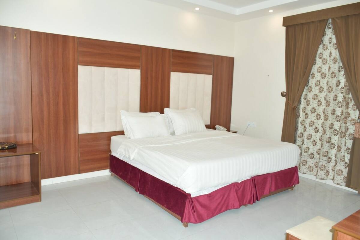A hotel room with a large bed, wooden headboard, and a small bedside table.
