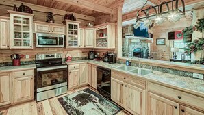 A wooden cabin-style kitchen with built-in appliances, a granite countertop, and a hanging pot rack. - Amazing 4BR Cabin -HT, Fire Pit & Game Room-10 Mins from PF (Sevierville)