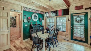 A wooden interior with a dining table, chairs, and a green wall with clocks. - Amazing 4BR Cabin -HT, Fire Pit & Game Room-10 Mins from PF (Sevierville)