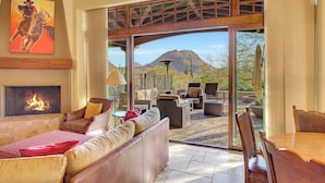 Un vaste espace de vie doté d’une cheminée, de sièges confortables et d’une grande porte vitrée donnant sur une terrasse extérieure avec vue sur les montagnes.