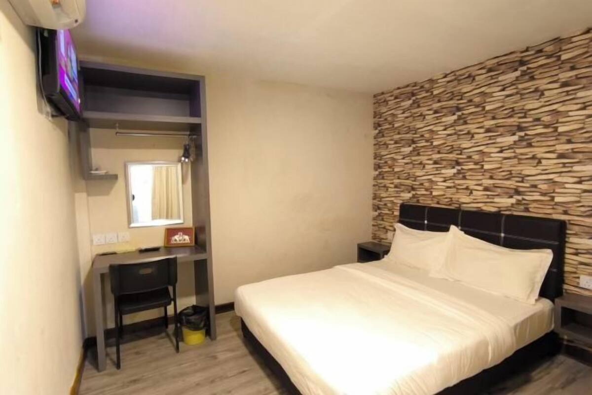 A bedroom with a bed, a desk with a chair, a television, and a stone-patterned wall.