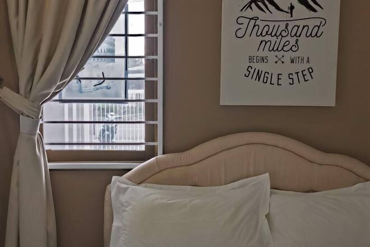 A bedroom with a bed, a window with blinds, and a wall with a motivational quote.