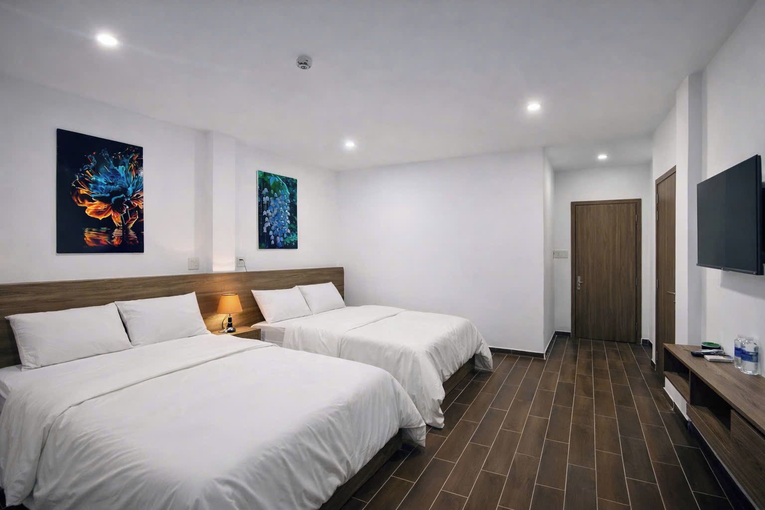 A hotel room with two beds, a TV, and artwork on the walls.