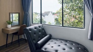 Un dormitorio moderno con un sofá de cuero negro curvo, un escritorio de madera y un amplio ventanal con cortinas.