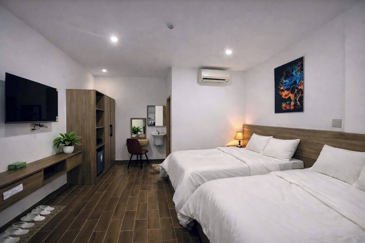 A hotel room with two beds, a desk, a TV, a bathroom, and a painting on the wall.