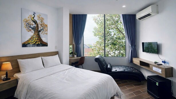 Habitación de hotel con cama, escritorio, silla, televisión y ventana con cortinas.