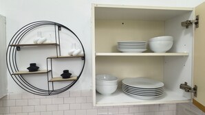 A kitchen with white tiled backsplash, a circular black metal shelf with white and black items, and a cabinet with stacked white bowls and plates.