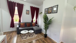 A modern living room with a grey sectional sofa, two white round tables, a patterned rug, and red curtains.