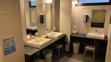 A modern bathroom with two sinks, mirrors, and a trash bin. There is a sign instructing to put used towels there.