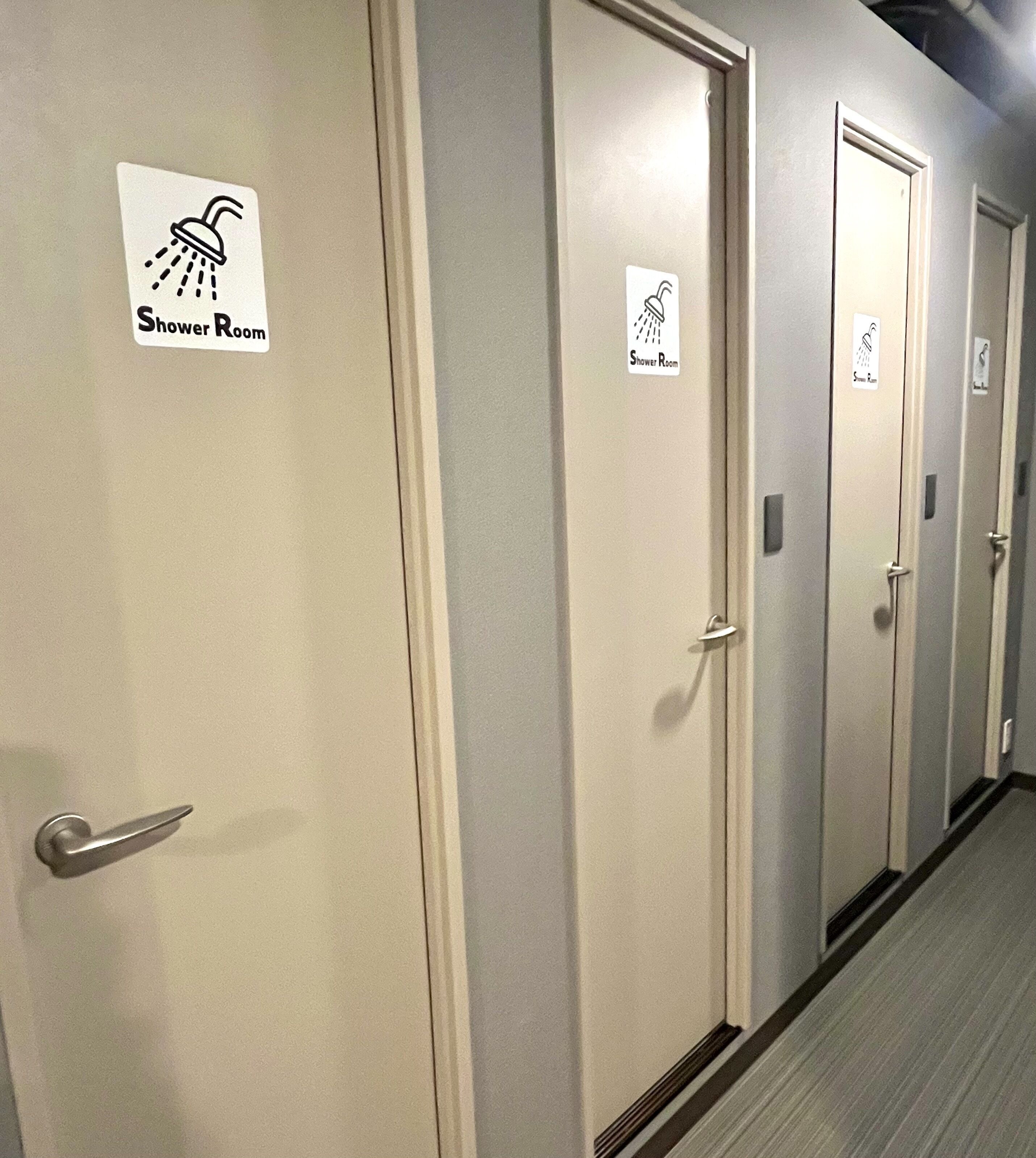 Een rij deuren met bordjes 'Douche ruimte', wat een hotelbadkamerzone aangeeft.