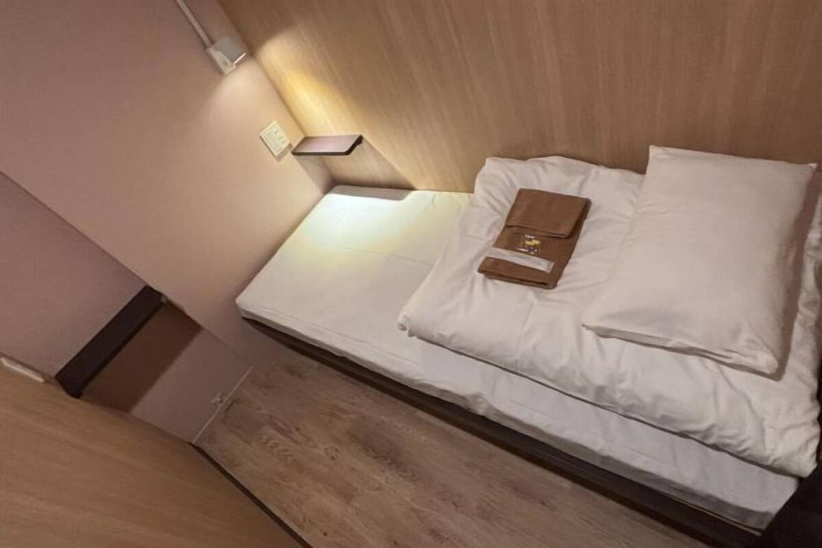 A bed with white linens, a bedside table, and a wall-mounted light.