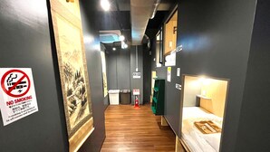 Un pasillo estrecho con suelo de madera que conduce a una habitación con cama. Un cartel de 'No Fumar' es visible en la pared izquierda.