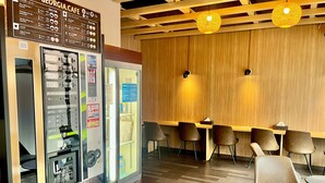 Interior de una cafetería con máquina expendedora, paneles de madera y zona de estar.