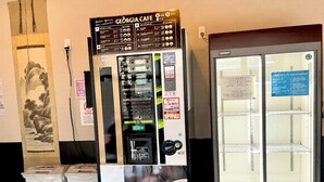 Máquina expendedora con publicidad de una taza de café, un refrigerador y botes de basura.