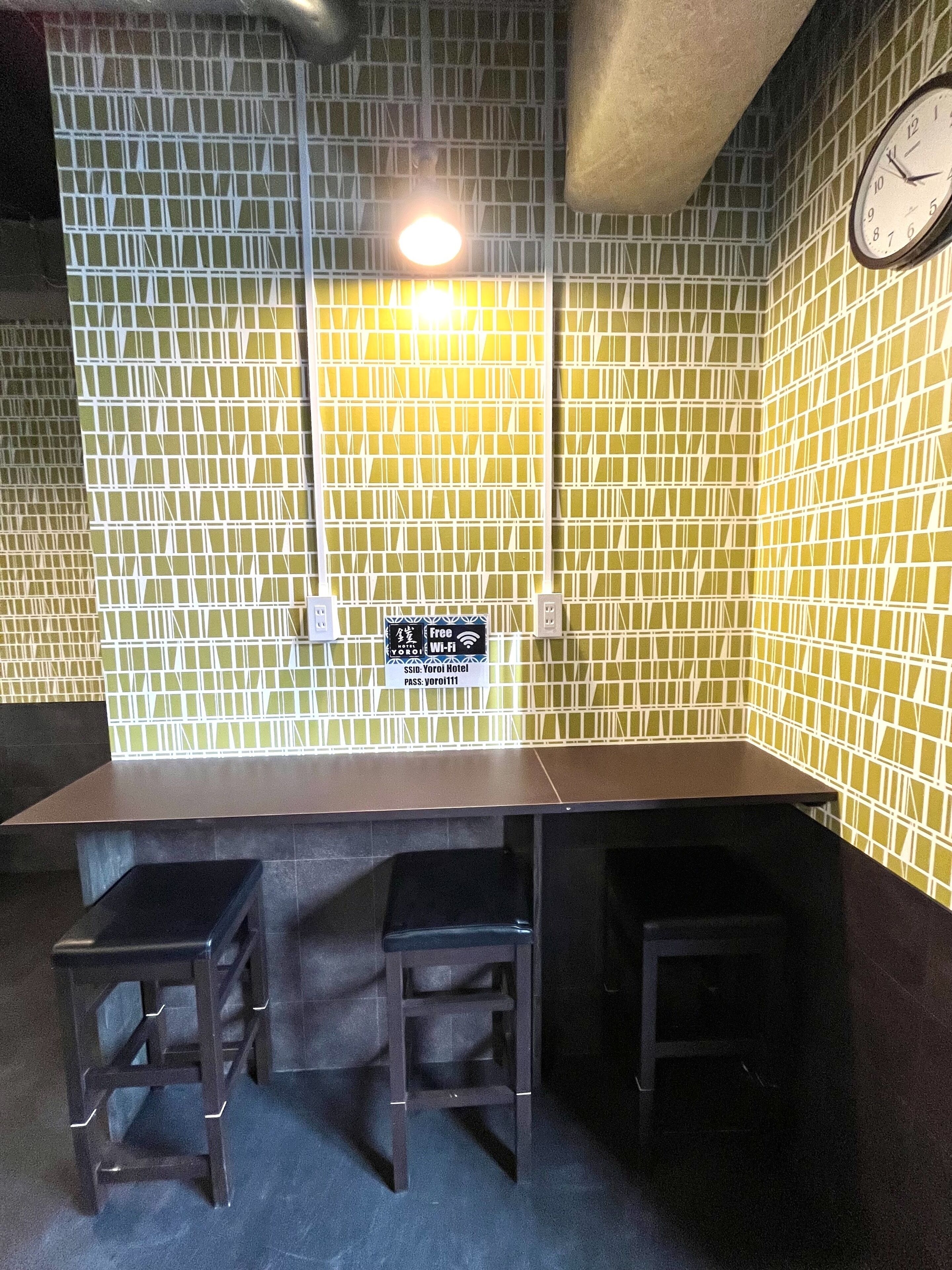 A corner room with a table and two stools, a clock on the wall, and a sign indicating free Wi-Fi.