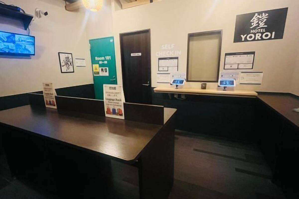 A hotel reception area with a self-check-in desk, a room number sign, and a 'Hotel Yoroi' sign.