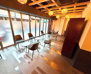 A modern interior with a mix of seating arrangements, including round tables and chairs, and a wooden ceiling with hanging lights. - Yoroi Asakusa Hotel (Tokyo)