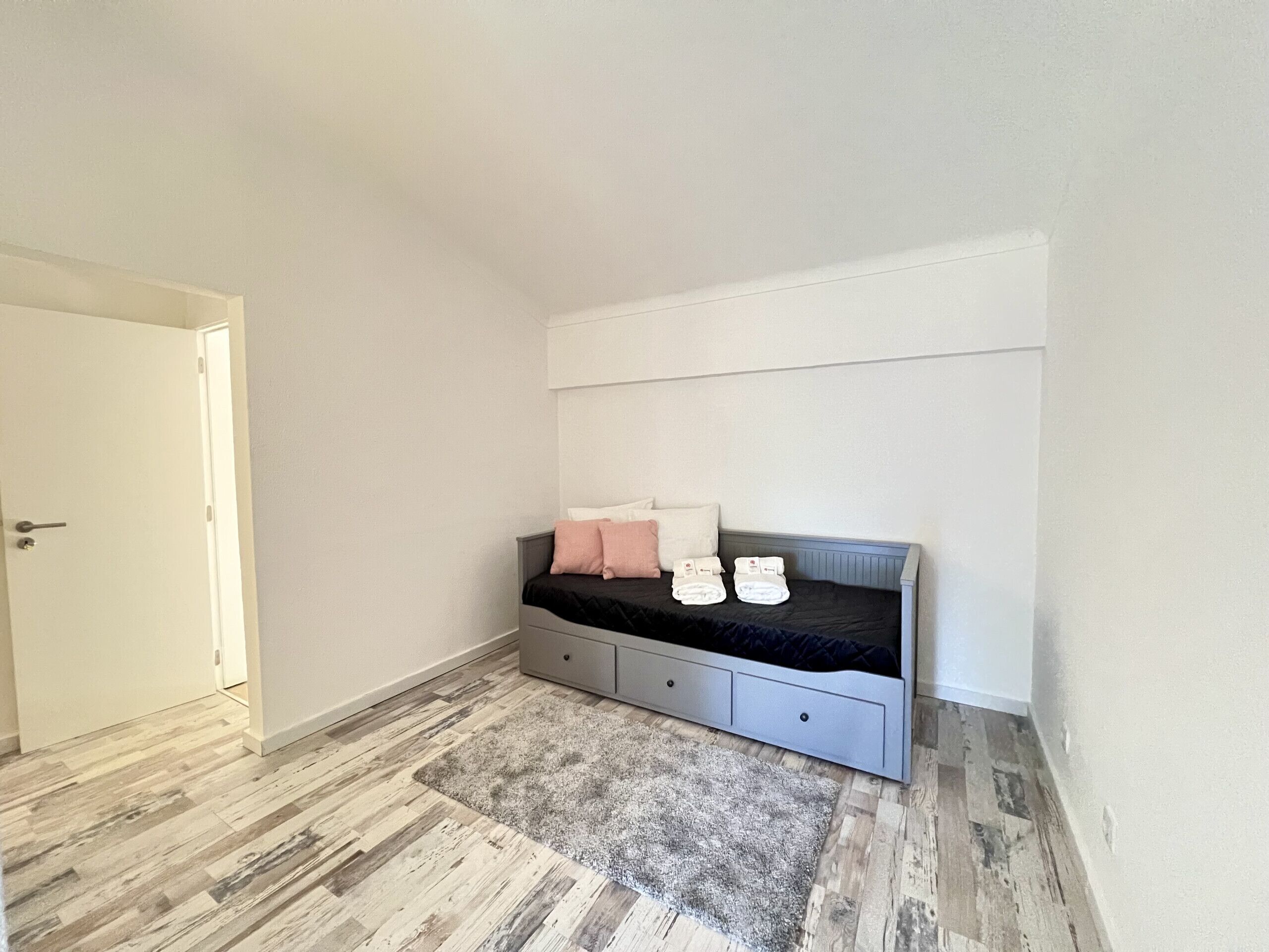 A bedroom with a bed, a grey headboard, a white door, and a grey rug.