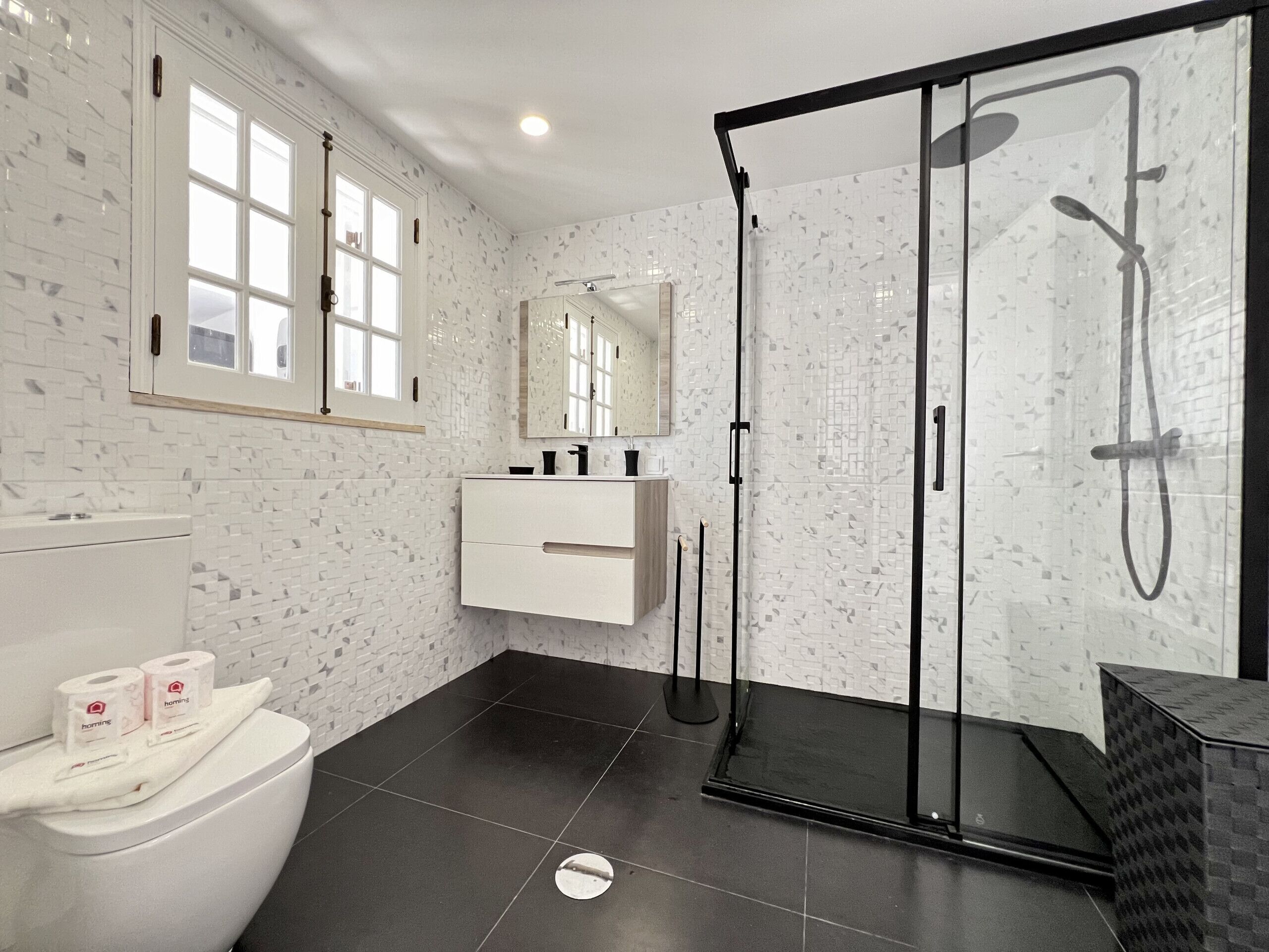 A modern bathroom with a glass-enclosed shower, a white toilet, and a vanity with a mirror.