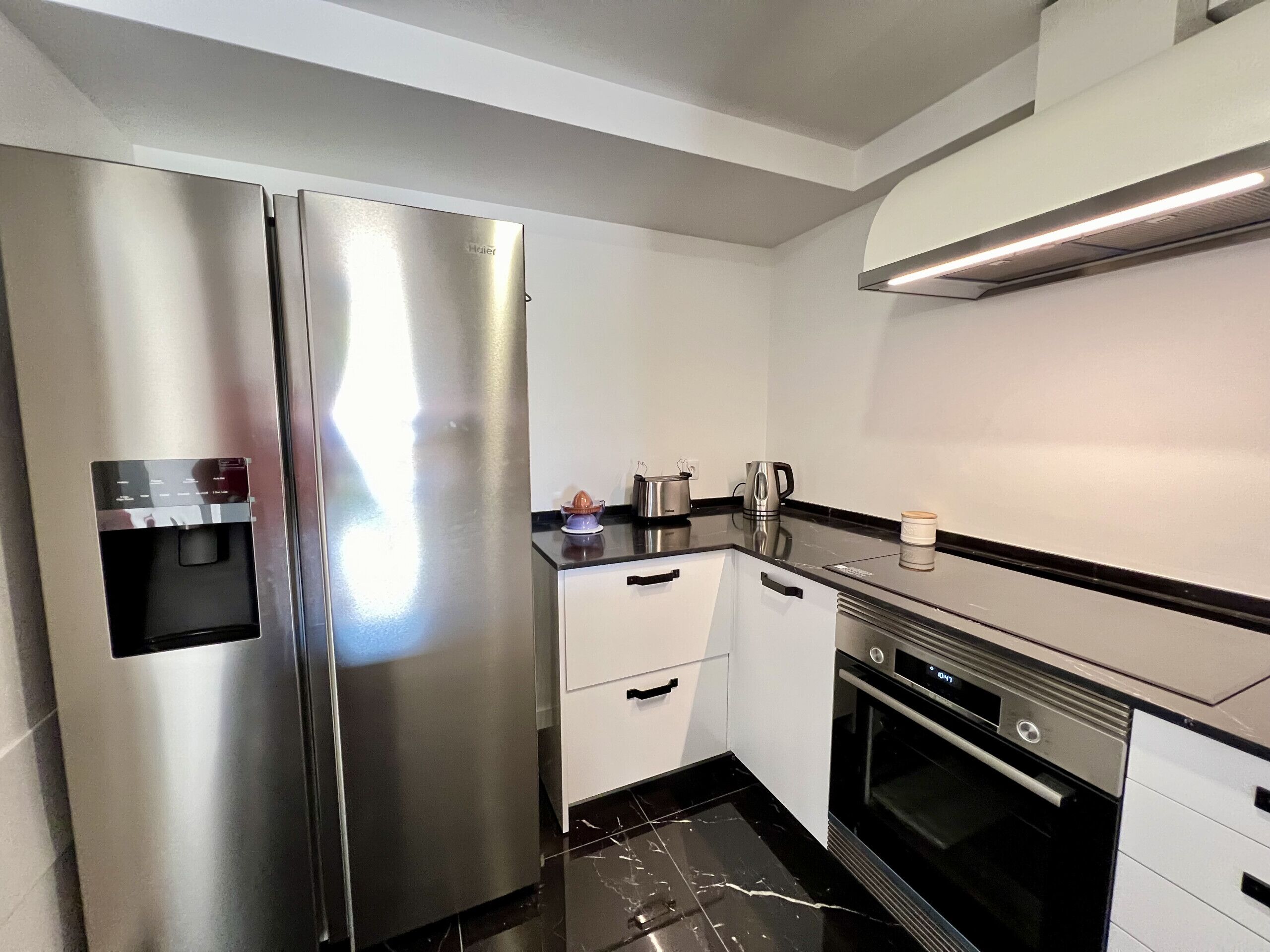 A modern kitchen with a stainless steel refrigerator, a built-in oven, and a coffee maker on the counter.